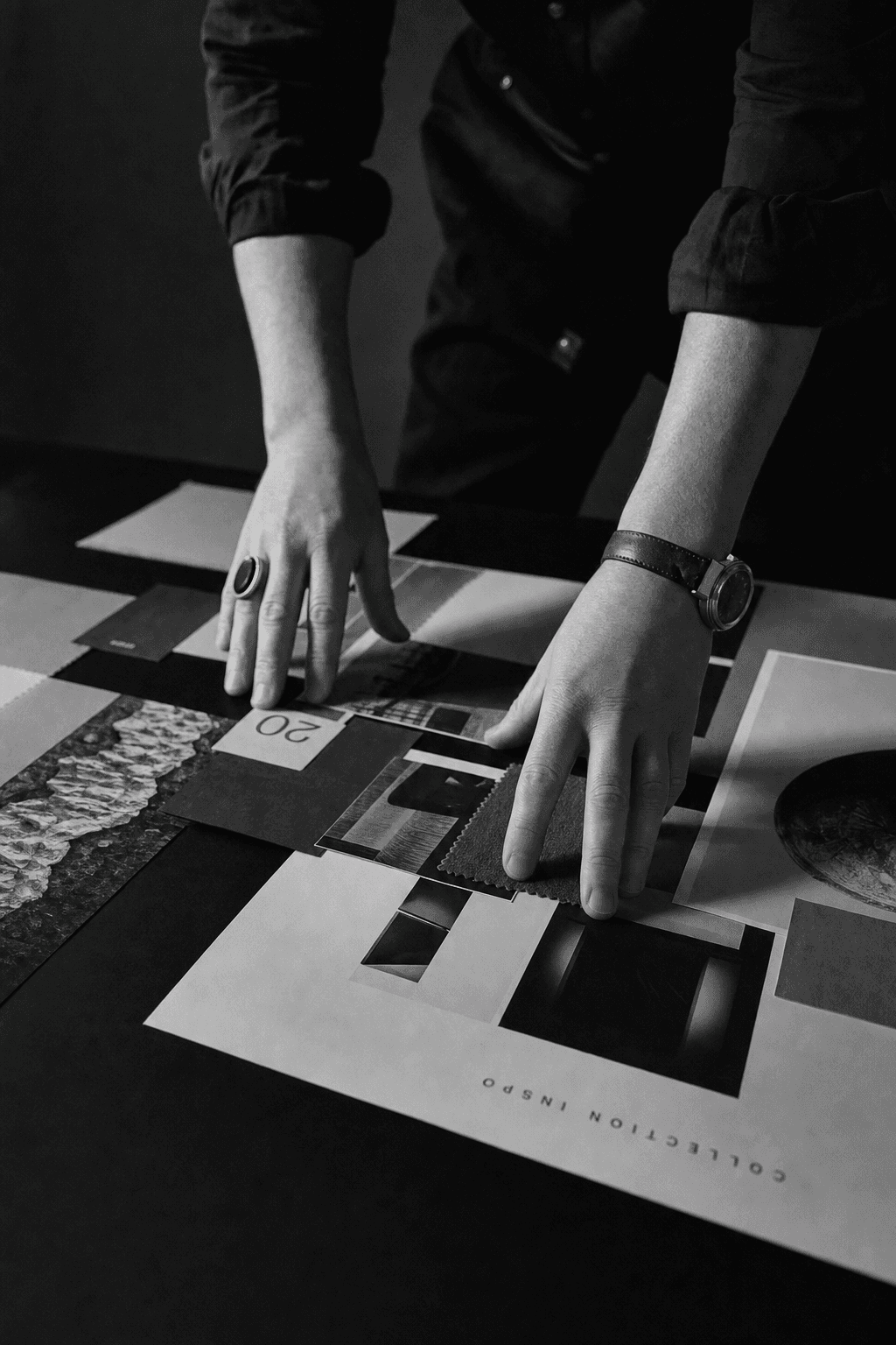 Editorial black and white photograph of a creative director's hands arranging layout sheets